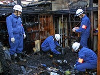 住宅火災が発生し、火災調査員が建物の床上付近の出火元を確認している。