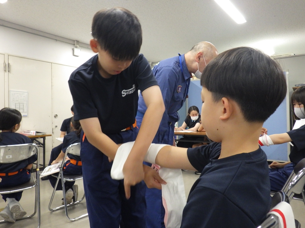 <三角巾を使用した応急救護訓練のようす>救急章2級の取得に向けて、三角巾の使い方を覚えました。 三角巾でしっかりと傷口を圧迫することで、上手に止血することが出来ました。